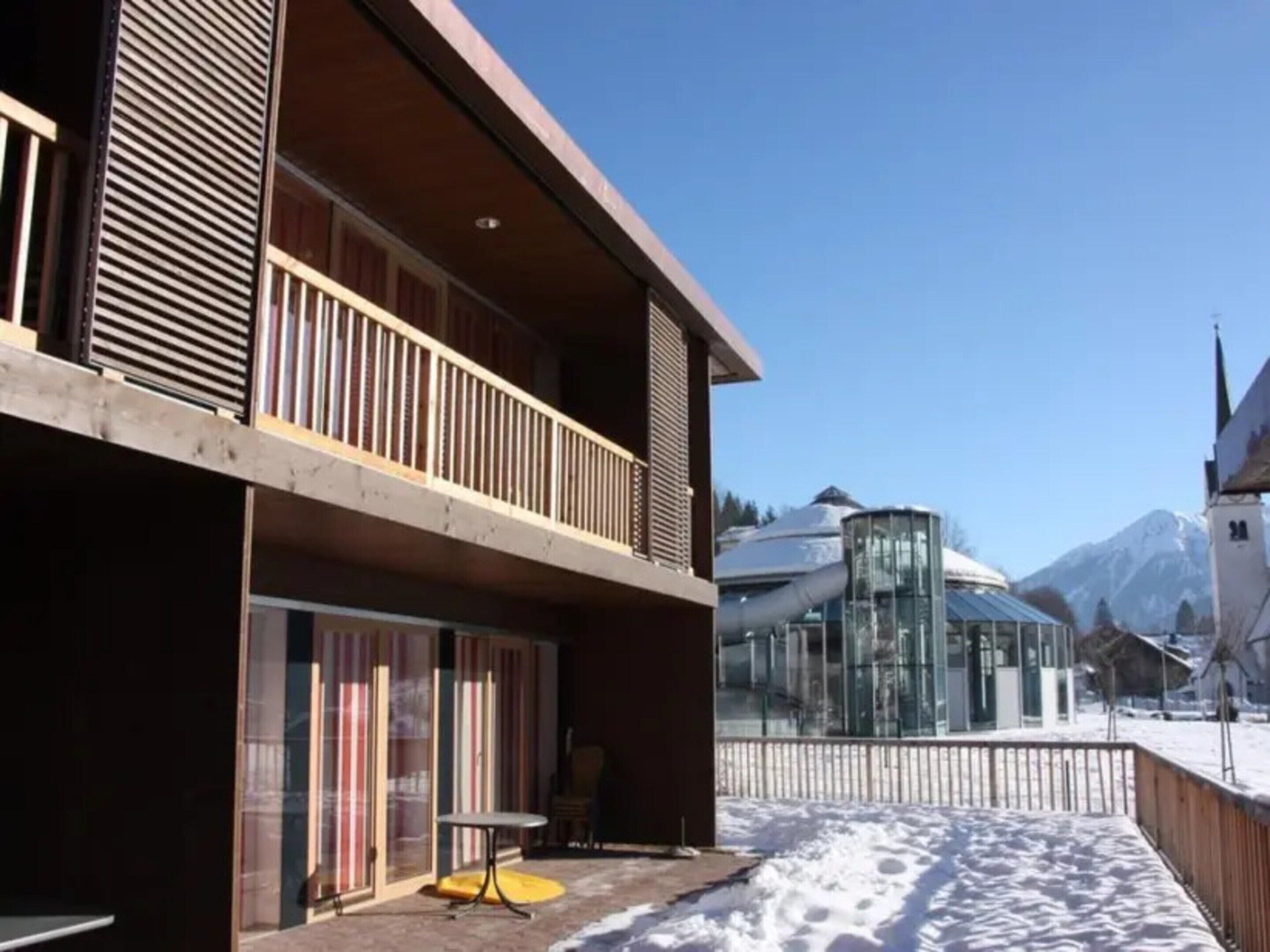 A modern building with a balcony, large windows, and a snowy ground.