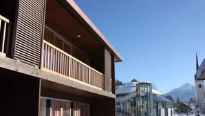 A modern building with a balcony, large windows, and a snowy ground. - Zirbenholz Alpine Maisonette Stay (Wald im Pinzgau)