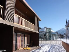 A modern building with a balcony, large windows, and a snowy ground. - Zirbenholz Alpine Maisonette Stay (Wald im Pinzgau)