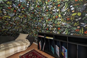 Une pièce avec un papier peint à motifs floraux, un lit, une bibliothèque et un tapis.