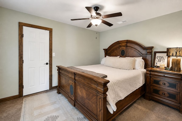 A bedroom with a wooden bed, a nightstand, a ceiling fan, and a door. - Reverie Reserve—5BR on Private Acre, North Keller (Keller)