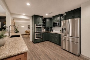 Une cuisine moderne avec des meubles de couleur vert foncé, des appareils en acier inoxydable et un plan de travail en granit.