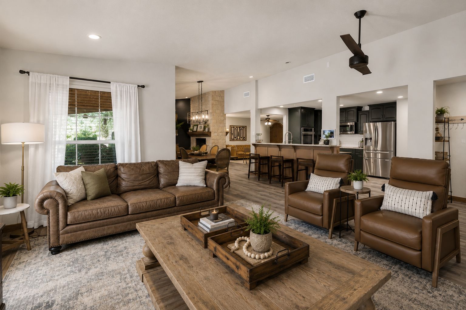 A modern living room with a brown leather sofa, a wooden coffee table, and a dining area with a stone fireplace.