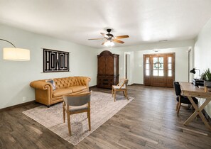 Un salon spacieux avec un canapé en cuir, un meuble en bois, une table à manger avec des chaises et un ventilateur de plafond.