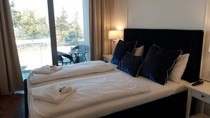 A hotel room with a large bed, a nightstand, a lamp, and a view of the outdoors. - Comfortable Apartment With a sea View (Miedzyzdroje)