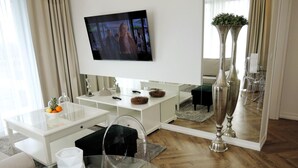 A modern living room with a flat-screen TV mounted on the wall, a glass coffee table, a white console table, and a large mirror reflecting the room. - Comfortable Apartment With a sea View (Miedzyzdroje)