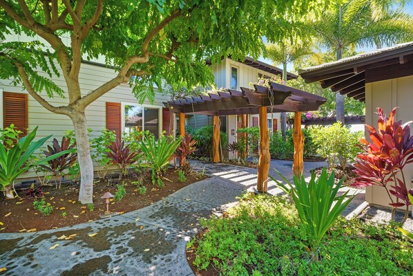 A garden with a pergola, various plants, and a pathway leading to a building with a covered porch. - Castle at Mauna Lani Golf Villas - A3 (Kamuela)