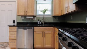 A kitchen with wooden cabinets, a stainless steel dishwasher, a gas stove, and a window with a plant. - Spacious 4-bedroom townhome in St. Louis  (St. Louis)