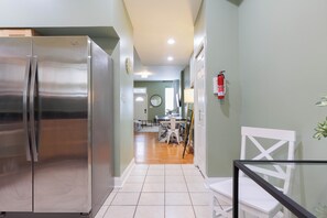 A kitchen with a stainless steel refrigerator, a dining area with a table and chairs, and a hallway leading to a living room.