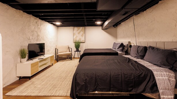 A modern bedroom with a large bed, a TV on a white cabinet, a small table with a plant, and a chair. - Spacious 4-bedroom townhome in St. Louis  (St. Louis)