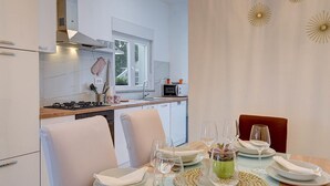 Eine moderne Küche mit weißen Schränken, einem Herd und einer Mikrowelle. Es gibt einen Essbereich mit einem Tisch für zwei Personen, komplettiert mit weißen Tellern, Gläsern und einer gewebten Tischmatte.
