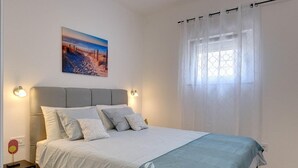 Ein Schlafzimmer mit einem Bett, einem Nachttisch, einer Lampe, einem Gemälde und einem Fenster mit Vorhängen.