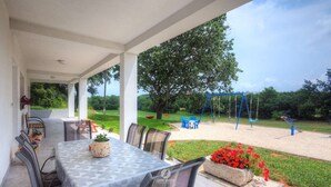 Eine Terrasse im Freien mit Tisch und Stühlen, ein Garten mit Blumen und ein Spielplatz im Hintergrund.