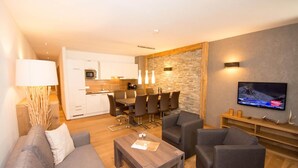 Ein modernes Wohnzimmer mit einer Couch, einem Couchtisch und einem Fernseher. Es gibt eine Küchenzeile mit einem Esstisch und Stühlen.