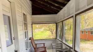 Un porche cubierto con una mesa y sillas, una puerta y una vista de una casa al fondo.