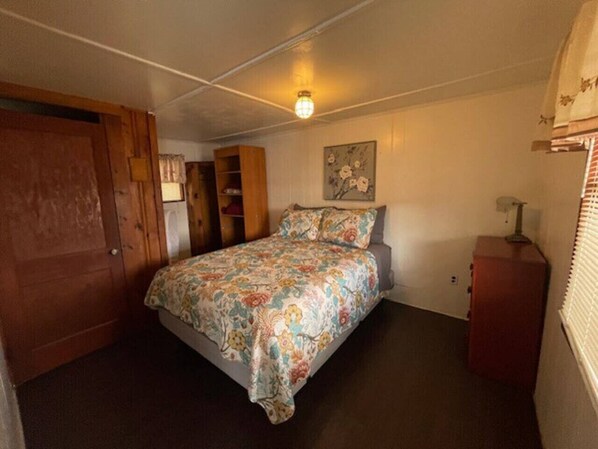 Une chambre à coucher comprenant un lit, une armoire en bois, une table de chevet et une lampe fixée au mur.