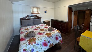 Een slaapkamer met een bed, nachtkastje, dressoir, stoel en een klein tafeltje.