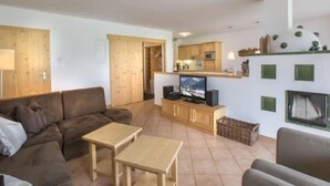 A living room with a sofa, two small tables, a television, and a kitchen area with cabinets and a microwave. - Maisonette Stay for 8 Guests (Wald im Pinzgau)