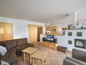 En stue med sofa, to små borde, et fjernsyn og et køkkenområde med skabe og en mikrobølgeovn.