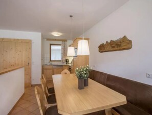 A dining area with a wooden table and chairs, a brown sofa, and a kitchen in the background. - Maisonette Stay for 8 Guests (Wald im Pinzgau)