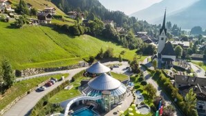 A resort with a swimming pool, a circular water slide, and a church in the background. - Maisonette Stay for 8 Guests (Wald im Pinzgau)