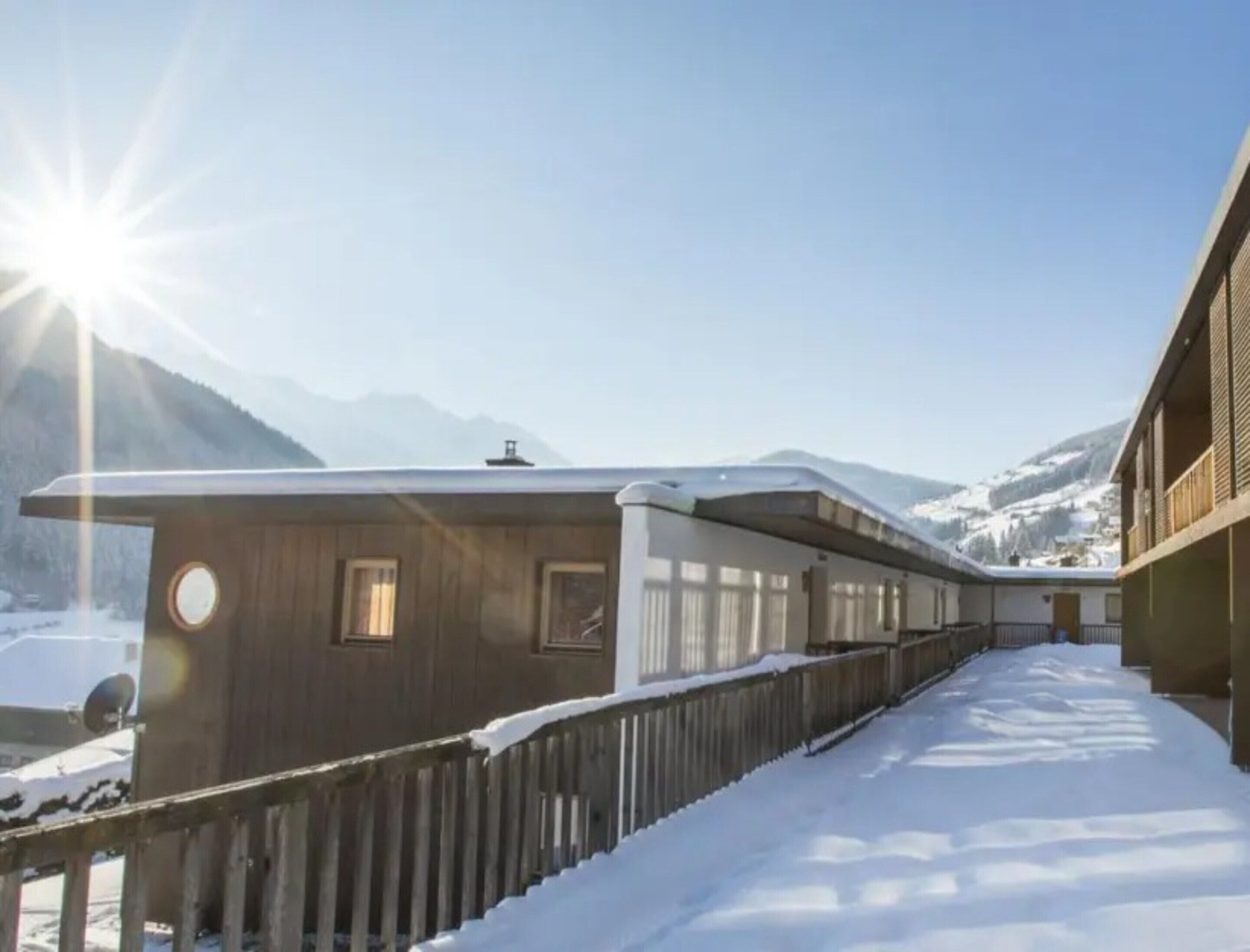 Un sentier enneigé mène à un bâtiment doté d’une façade en bois et d’un balcon.