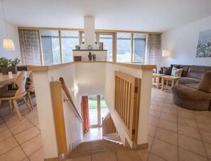 A spacious living area with a staircase leading to a balcony, a dining area with chairs, and a couch. - Maisonette Stay for 8 Guests (Wald im Pinzgau)
