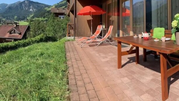 A patio with a table and chairs, a red umbrella, and a view of mountains. - Maisonette Stay for 8 Guests (Wald im Pinzgau)