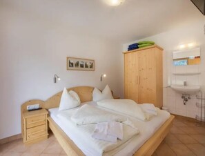 A bedroom with a bed, bedside table, wooden wardrobe, and a bathroom with a sink. - Maisonette Stay for 8 Guests (Wald im Pinzgau)