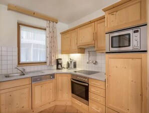 A kitchen with wooden cabinets, a microwave, a coffee maker, and a window with curtains. - Maisonette Stay for 8 Guests (Wald im Pinzgau)