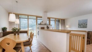 A modern kitchen with a dining area, large windows, and a wooden railing. - Maisonette Stay for 8 Guests (Wald im Pinzgau)