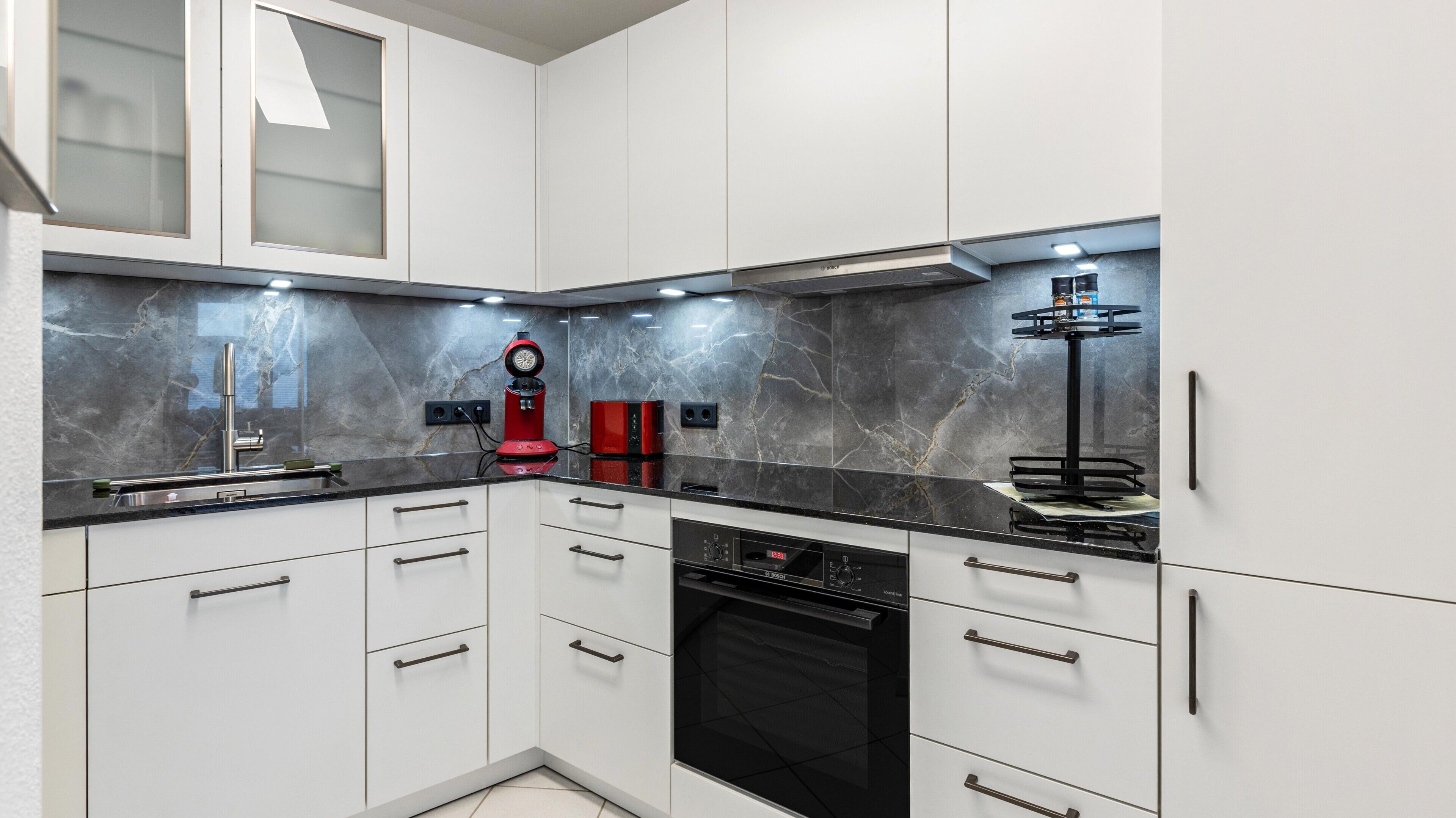 A modern kitchen with white cabinets, a black countertop, and a Bosch dishwasher.