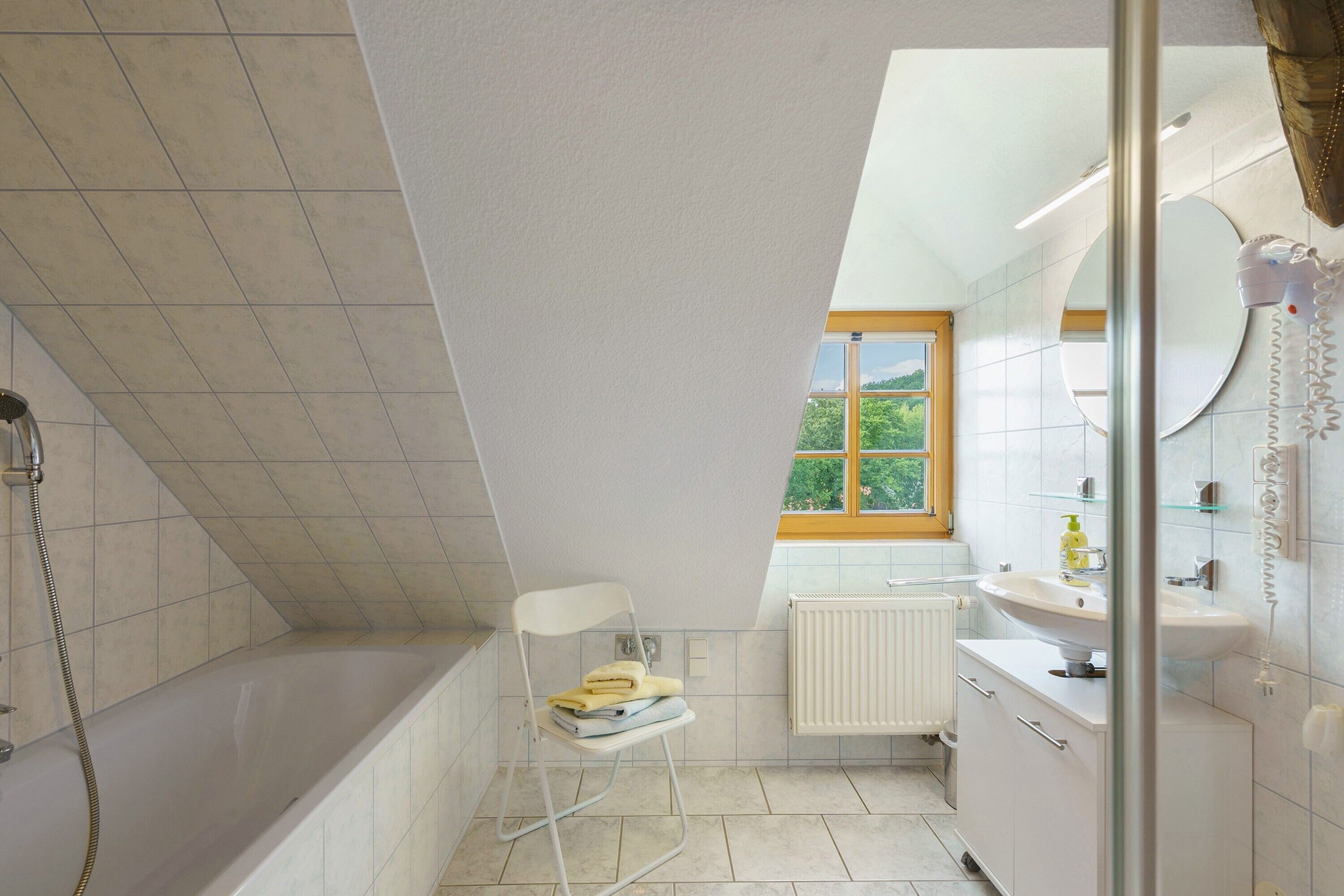 A bathroom with a bathtub, a shower, a window with a view, a radiator, and a sink.