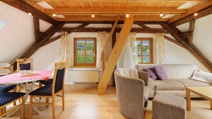 A cozy attic room with a wooden ceiling, a dining table with chairs, a sofa, and a window with curtains. - Apartment 'Gutshof Lesch - Ferienwohnung 2' with Private Garden and Wi-Fi (Chemnitz)
