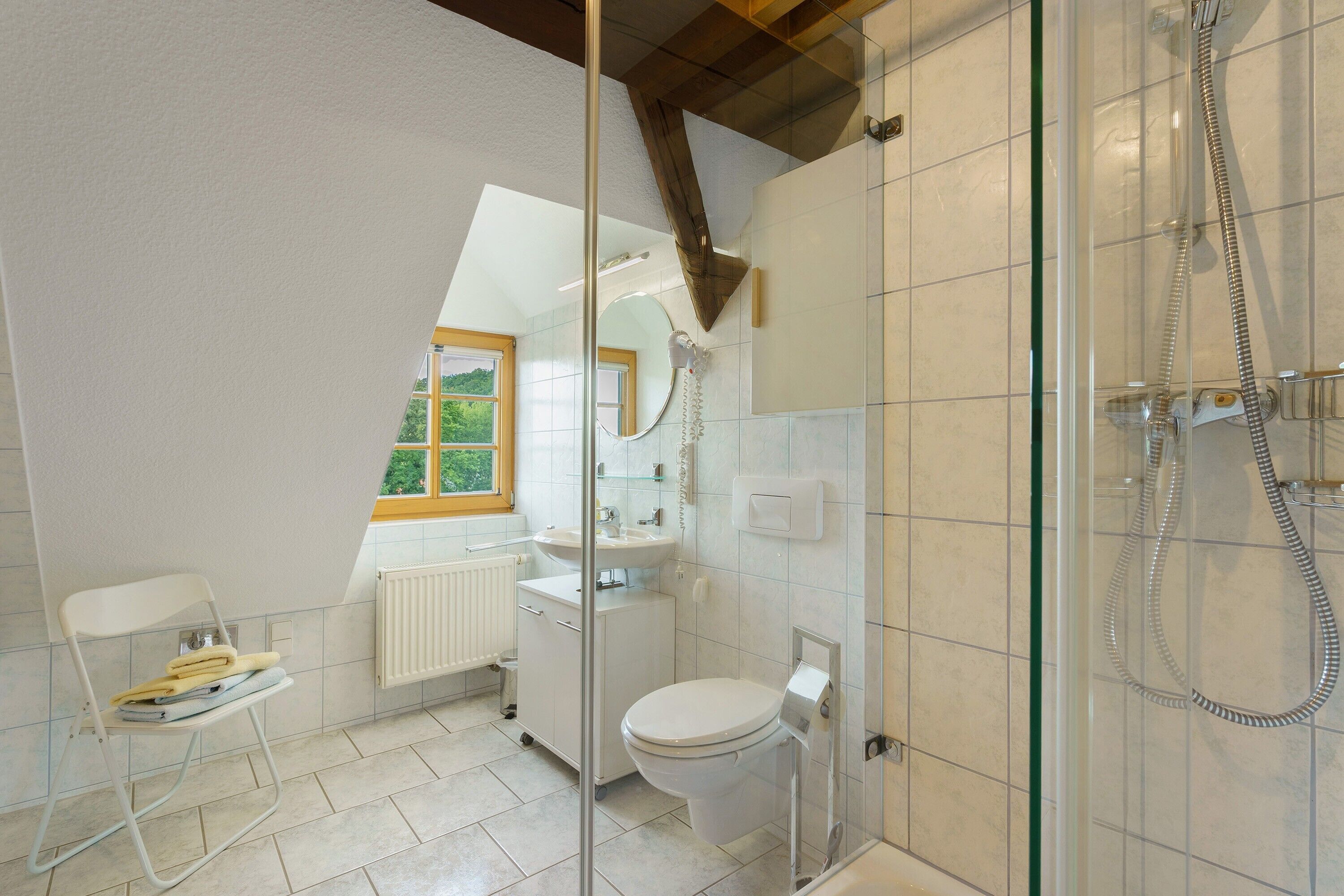 Une salle de bain équipée de toilettes, d’un lavabo, d’une douche et d’une fenêtre donnant sur un paysage agréable.