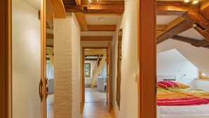 A narrow hallway with wooden beams and a sloped ceiling, leading to a bedroom with a bed and pillows. - Apartment 'Gutshof Lesch - Ferienwohnung 2' with Private Garden and Wi-Fi (Chemnitz)