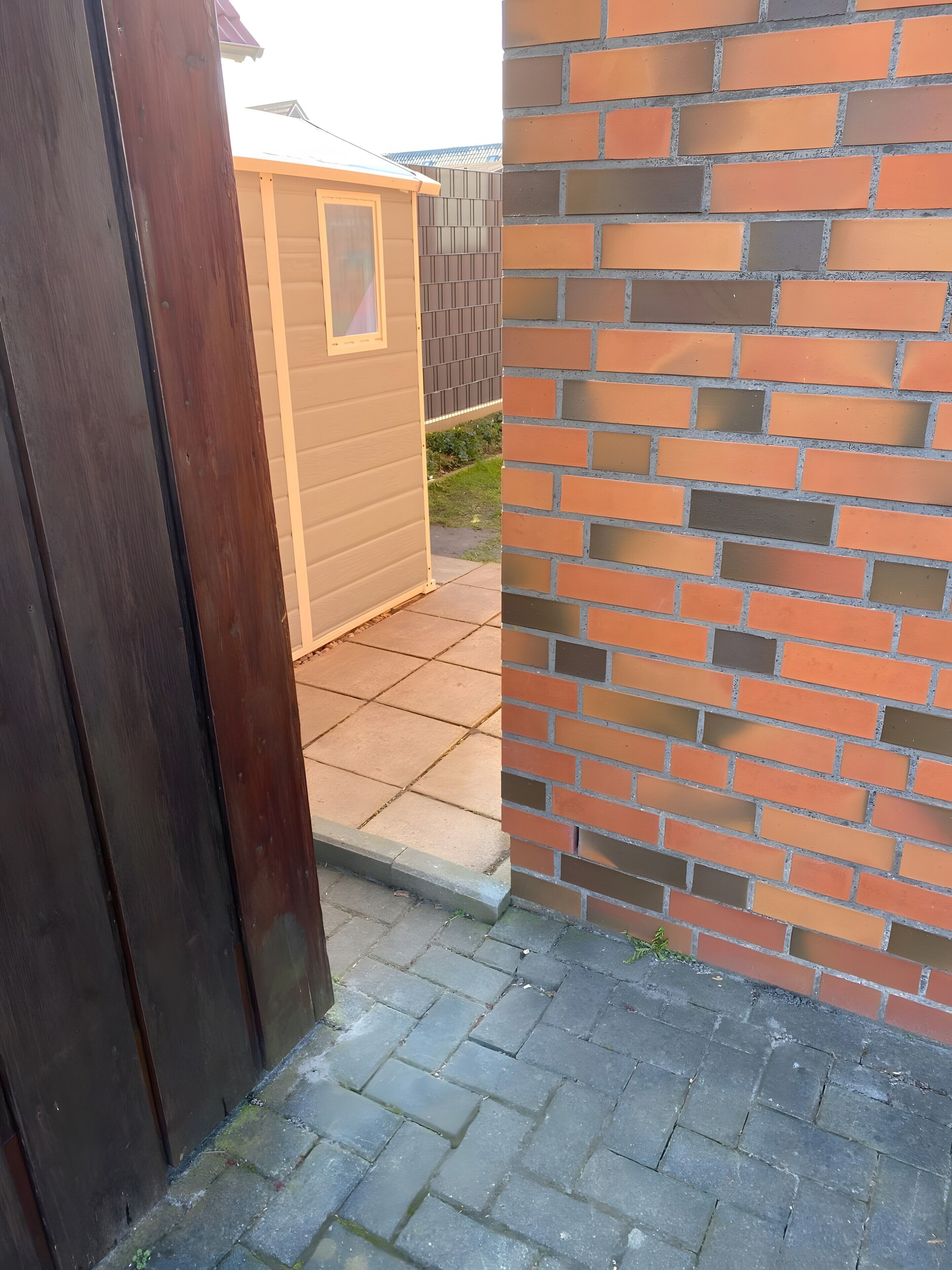 A wooden door, a brick wall, and a small shed with a window.