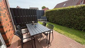Une terrasse avec une table et des chaises, un mur en briques, une haie et une clôture.