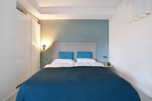 A bedroom with a bed, two pillows, a nightstand, a lamp, and a patterned wall. - Apartment 'Modernes  Ammersee' with Private Terrace, Private Garden and Wi-Fi (Windach)