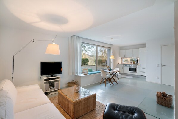 Una sala de estar moderna con un sofá, televisión y un comedor con mesa y sillas.
