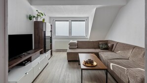 Ein modernes Wohnzimmer mit Flachbildfernseher, Holz-Unterhaltungseinheit, einer Couch, einem Couchtisch und einer Pflanze.