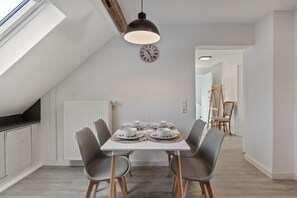 Un coin repas avec une table dressée pour quatre personnes, une horloge au mur et une vue sur un couloir.
