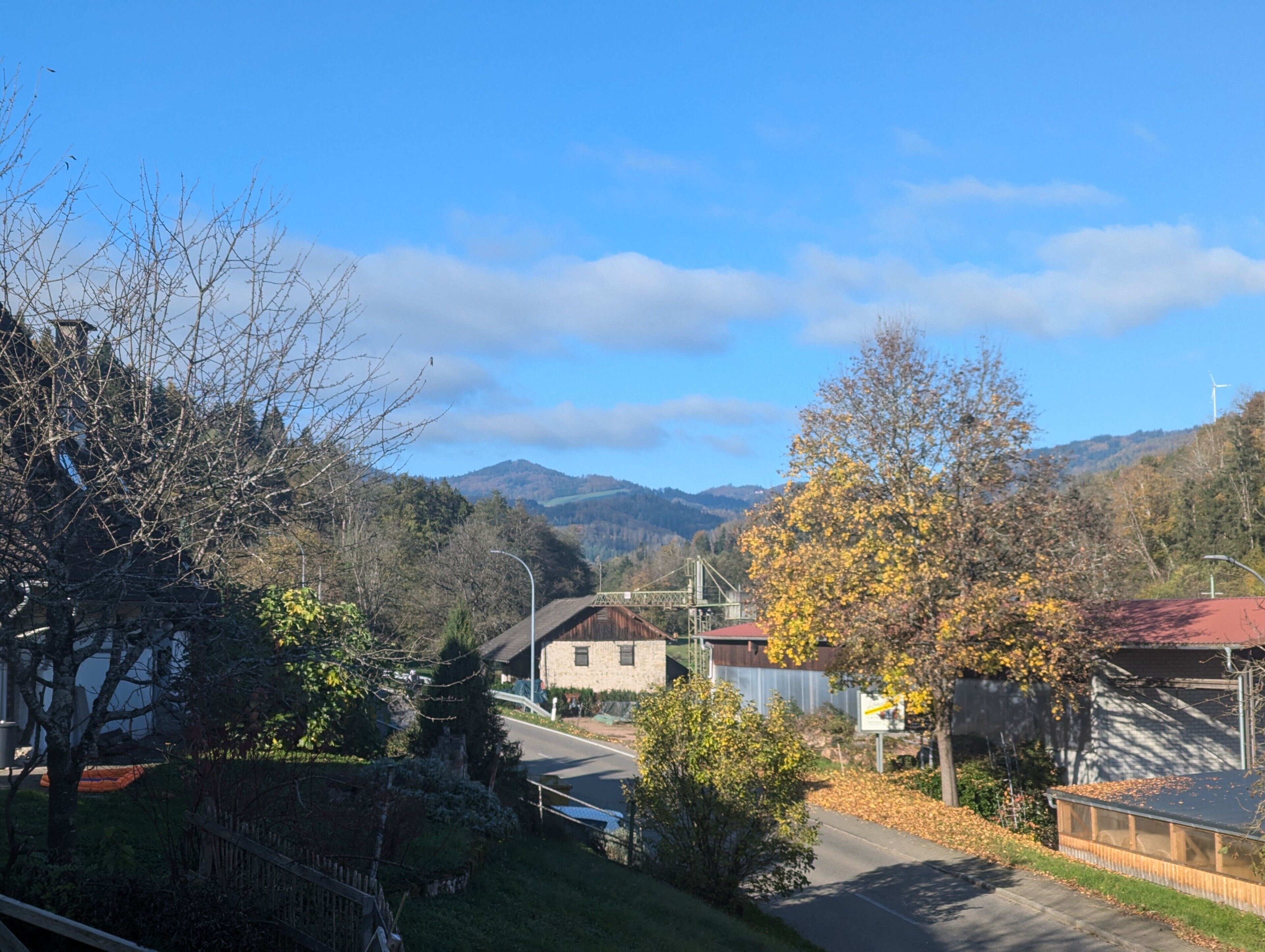 Une rue résidentielle bordée de maisons, avec un pont et des montagnes en arrière-plan.