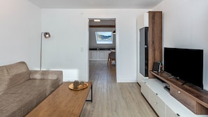 Ein modernes Wohnzimmer mit Sofa, Couchtisch, Fernseher und Blick in die Küche.