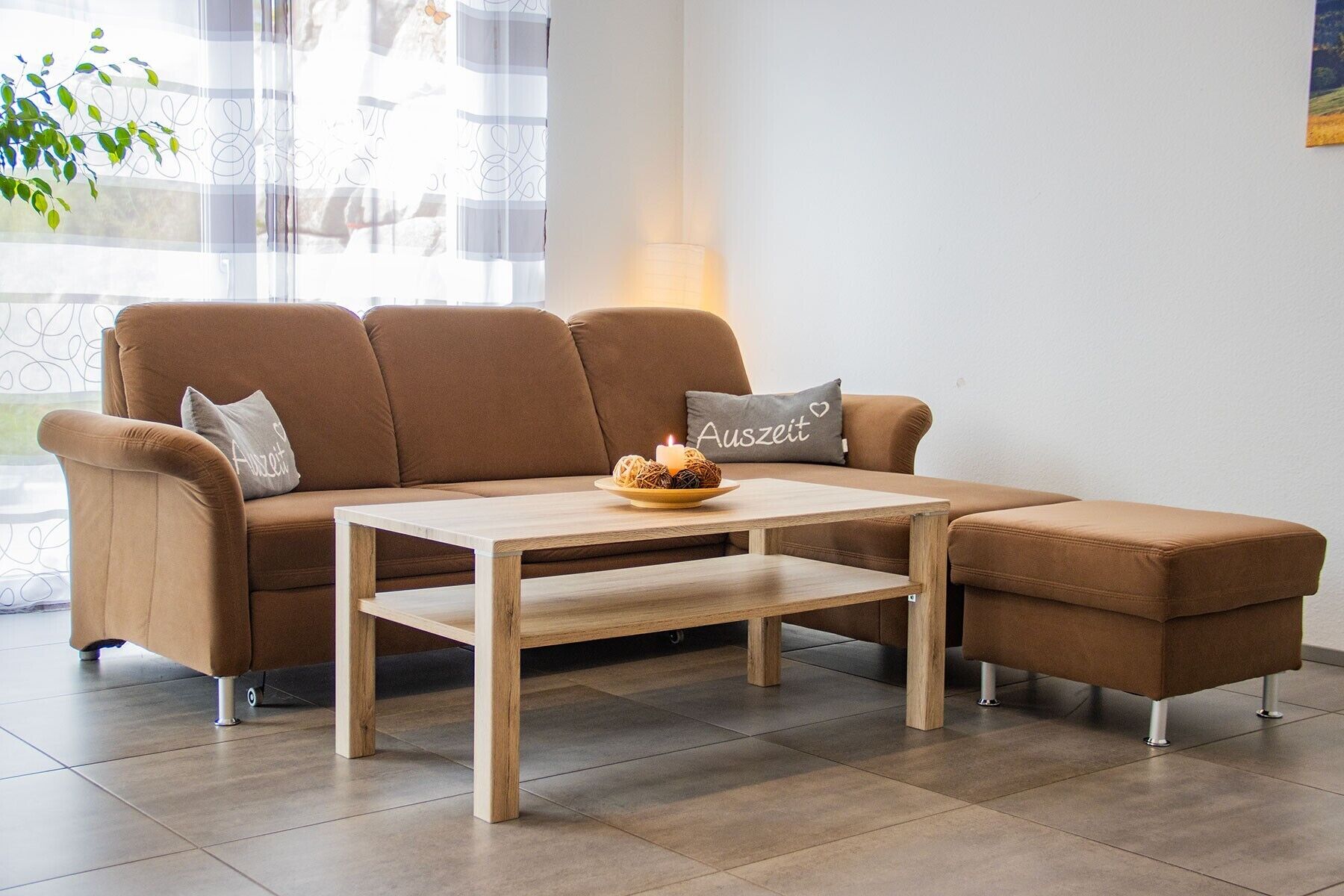 A brown sofa with a wooden coffee table, a cushion with 'Auszeit' text, and a candle on the table.