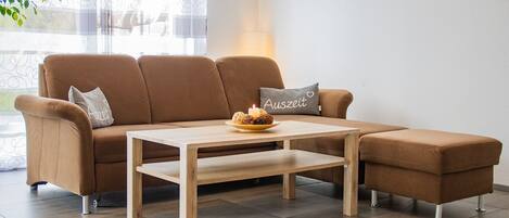 A brown sofa with a wooden coffee table, a cushion with 'Auszeit' text, and a candle on the table.