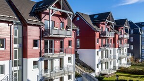 Une rangée d’immeubles d’appartements aux façades rouges et blanches, dotés de balcons, un ciel dégagé et une pelouse bien entretenue.