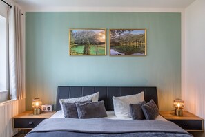Ein Schlafzimmer mit einem Bett, zwei Nachttischlampen, einem Kopfteil und zwei gerahmten Bildern an der Wand.
