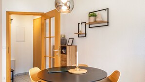 Un coin repas comprenant une table ronde, des chaises, un luminaire suspendu et une étagère murale agrémentée d’objets décoratifs.