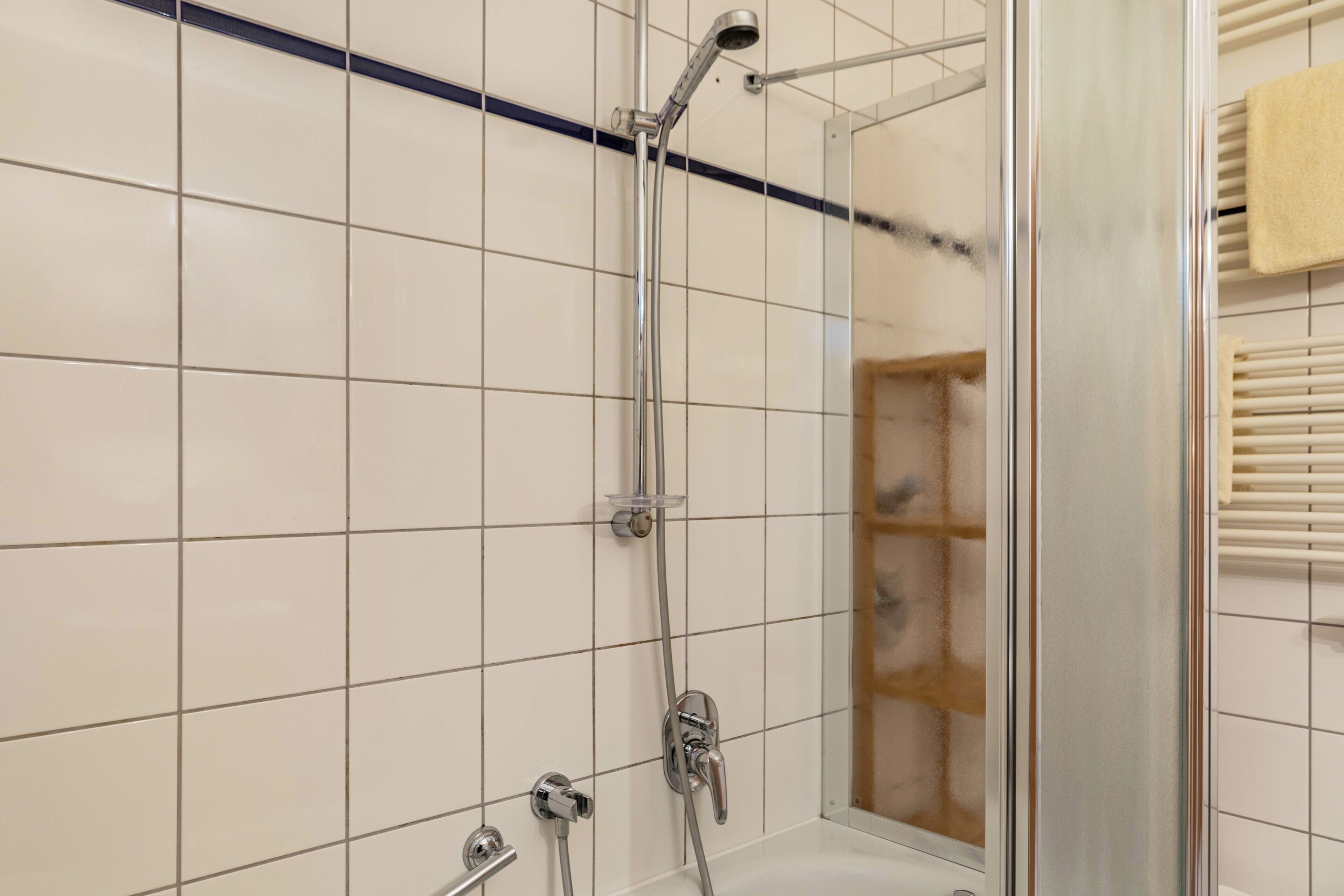 A shower with a glass enclosure, a towel rack, and a tiled wall.
